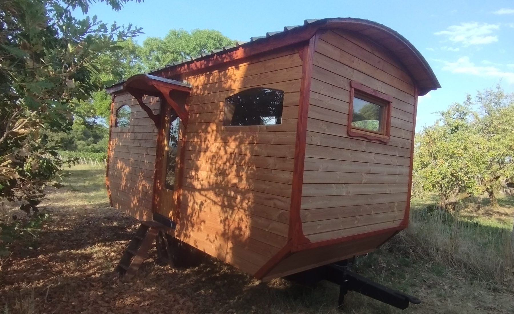 Roulotte en bois avec auvent, installée dans un verger